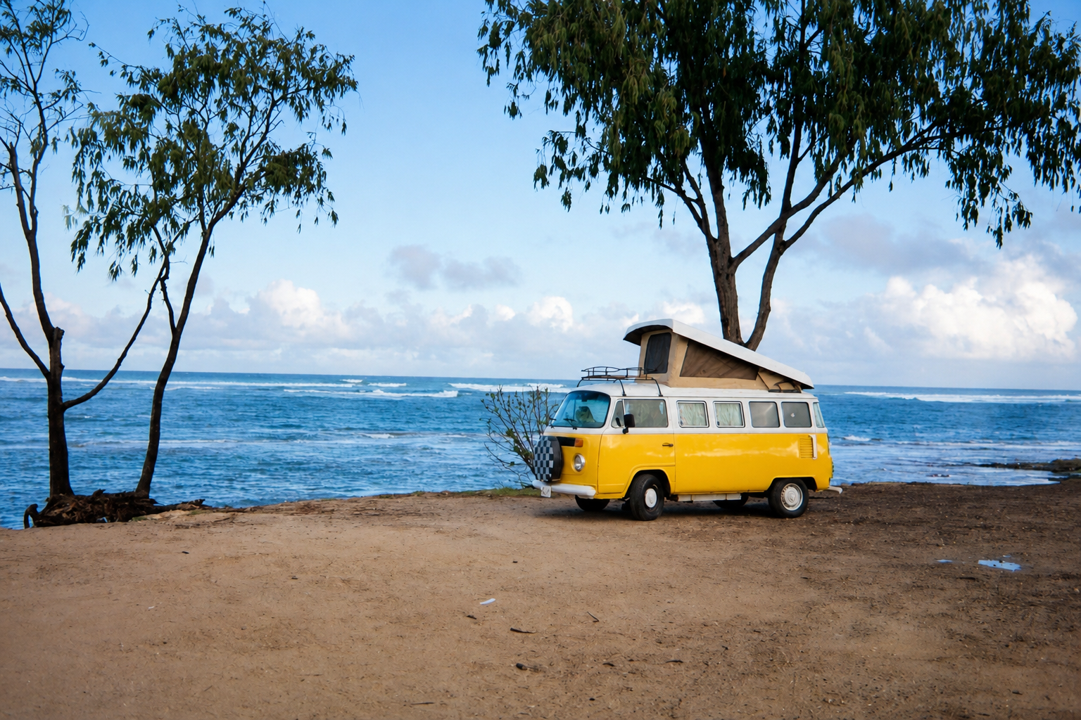 Yellow vintage camper van parked beside the ocean.
